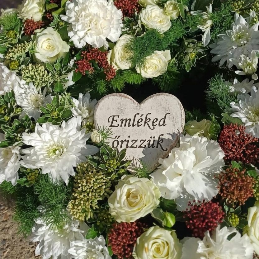 Szívkoszorú részlete fehér rózsákkal és szegfűkkel, közepén fa szívvel, amelyen az Emléked őrizzük felirat olvasható