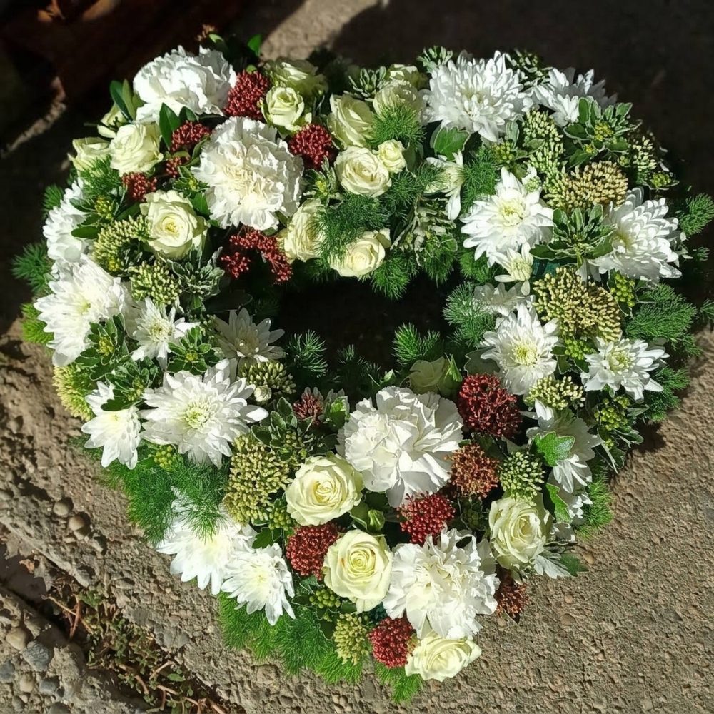 Élővirágos szívkoszorú fehér rózsával, szegfűvel és krizantémmal, vörös bogyós sziklevéllel és zöld díszítéssel